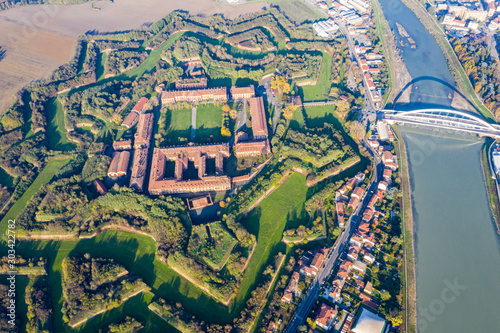 Aerial view of walls and bastions of modern six-star hexagon shaped fort Cittadella of Alessandria on winding river Tanaro. Piedmont, Italy. Bridge Ponte Meier connects fortress to town centre