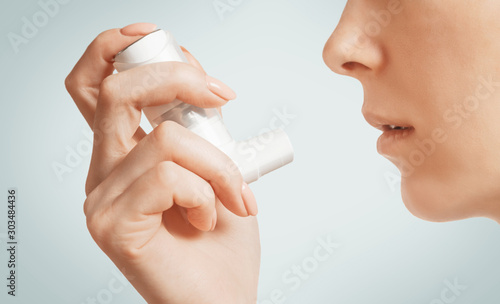 Woman holding medical asthma inhaler near her face.