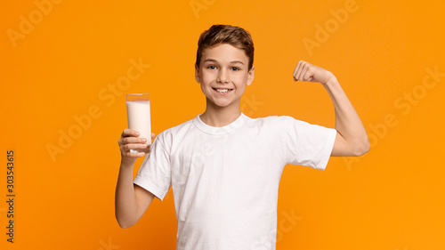Confident strong teenager enjoying milk and showing his biceps