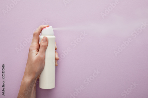 cropped view of woman spraying deodorant on violet background with white roses