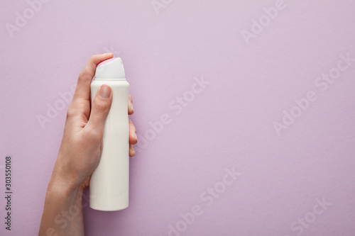 cropped view of woman holding spray deodorant on violet background with white roses