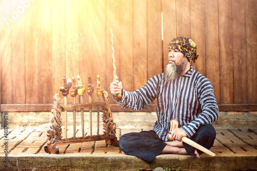 Asian old man showing his keris or kris collection with wooden wall background