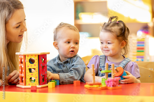 Nursery kids play with montessori toys in classroom. Kindergarten teacher looks after children