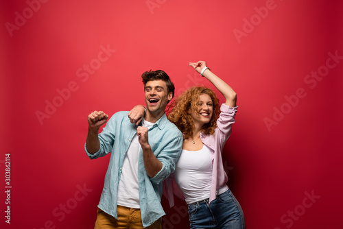 Beautiful excited couple dancing in casual clothes isolated on red