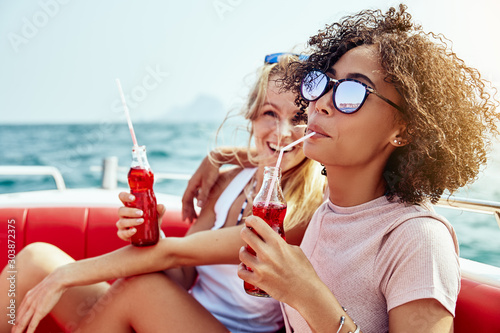 Two young female friends laughing over drinks on a boat