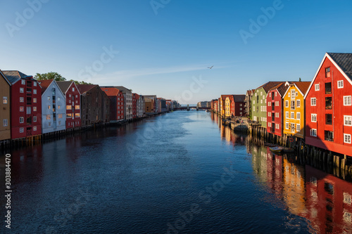 Historic timber buildings line the banks of the River Nidelva in Trondheim, Norway. July 2019, sunset.