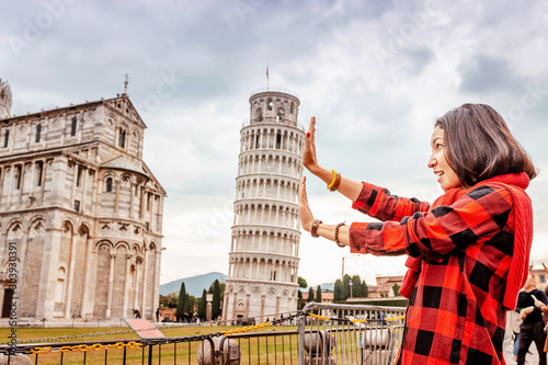 Funny Asian girl supporting famous leaning tower in Pisa. Travel concept