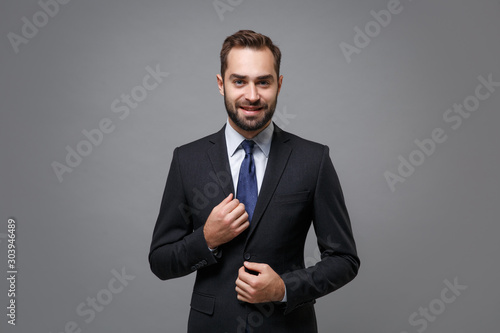 Smiling young bearded business man in classic black suit shirt tie posing isolated on grey background studio portrait. Achievement career wealth business concept. Mock up copy space. Looking camera.