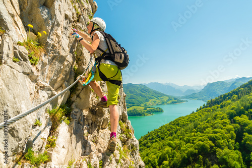 Beautiful young girl climbing Drachenwand via ferrata above scenic Mondsee lake, Alps, Austria, Europe