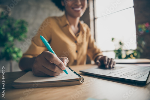 Cropped close up photo of cheerful positive girl in yellow shirt writing down essential details of online conference having just been held on laptop