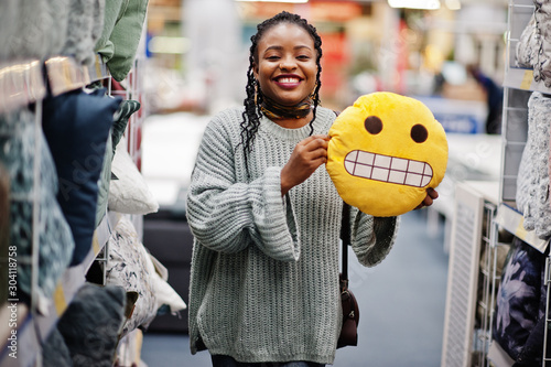 Face with teeth emoji. African woman with pillow in a modern home furnishings store.