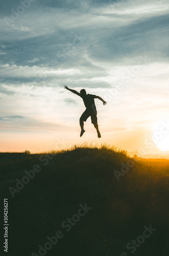 silhouette of young man jumping on sunset background of blue sky