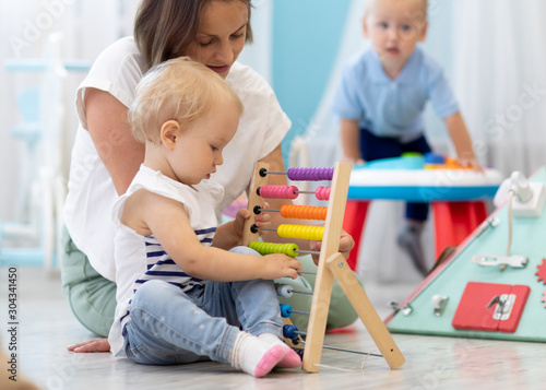 Kids playing on floor with developmental toys in kindergarten. Children have fun in nursery or daycare. Babies with teacher in creche