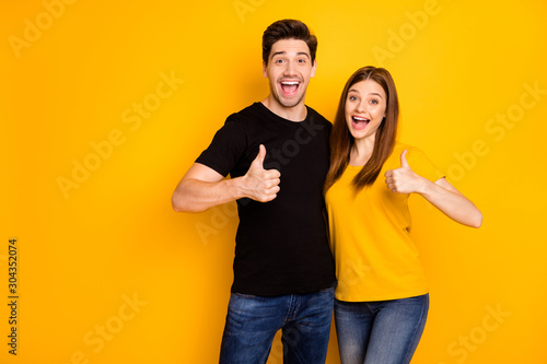 Photo of positive cheerful cute charming girlfriend and boyfriend showing their thumbs up wearing jeans denim black t-shrit expressing kind emotions giving feedback isolated vibrant color background