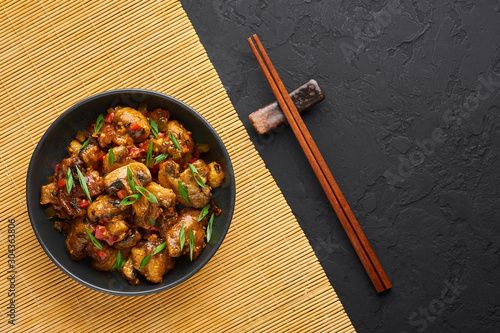 Mushrooms Manchurian dry in black bowl at dark slate background. Mushroom Manchurian - is indo chinese cuisine dish with deep fried mushrooms, bell peppers, sauce and onion.