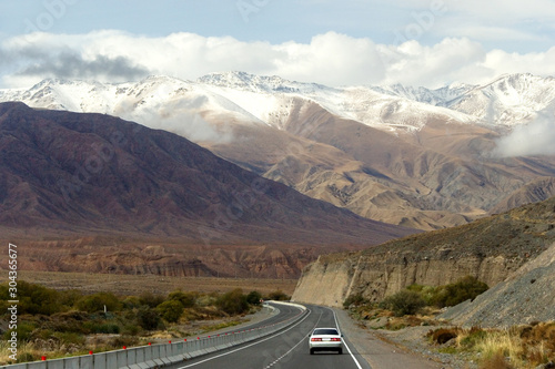 Highway with a car on a background of high mountains, some of which are covered with snow, Kyrgyzstan