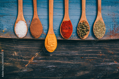 flat lay of colorful spices in spoons on wooden table with copy space. tumeric stands out