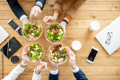 Office workers during a business lunch with healthy salads and coffee cups, view from above on the wooden table