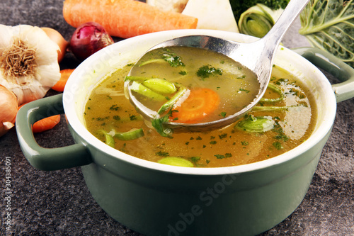 Broth with carrots, onions various fresh vegetables in a pot - colorful fresh clear spring soup. Rural kitchen scenery vegetarian bouillon stock