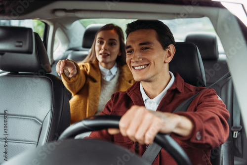 Smiling taxi driver with woman passenger pointing on road