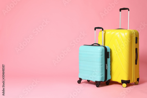 Stylish yellow and turquoise suitcases on pink background. Space for text