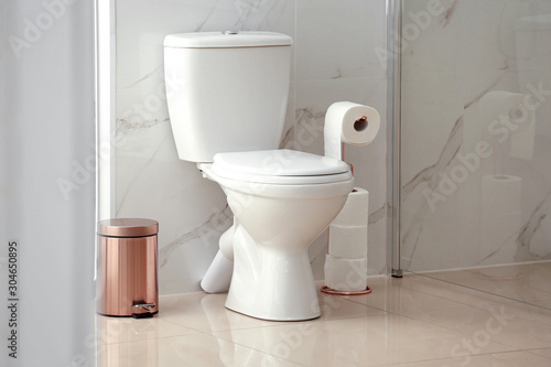 Modern toilet bowl with roll of paper in bathroom