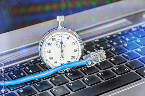 Cable and stopwatch on computer keyboard symbolizing bandwidth of internet connection