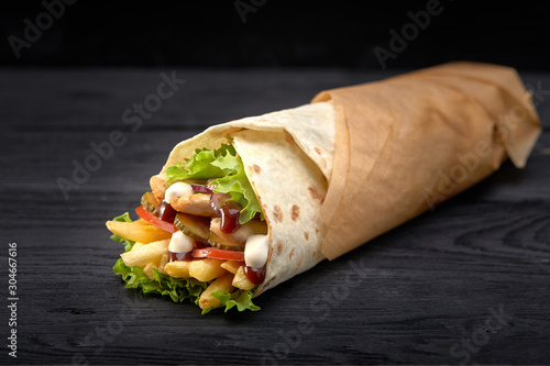 Tasty doner kebabs with fresh salad trimmings and shaved roasted meat served in tortilla wraps on brown paper as a takeaway snack