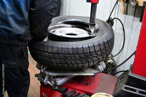 Concept Photography with a tire fitting. A worker is serving a car. He puts the tire on the wheel disc using a special machine and tool.