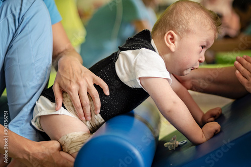 Portrait of a baby with cerebral palsy on physiotherapy in a children therapy center. Boy with disability has therapy by doing exercises. Little kid has musculoskeletal therapy in rehabitation centre.