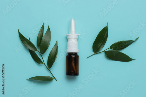 Herbal medicine. White pills, nasal spray with green leaves on blue background. Minimalistic medicine still life