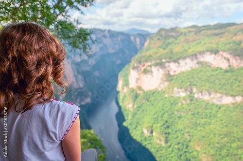 Young woman with typical Mexican blouse watching from the heights the Cañon Del Sumidero through which it crosses the Grijalva river, with monañas in the background and blue sky