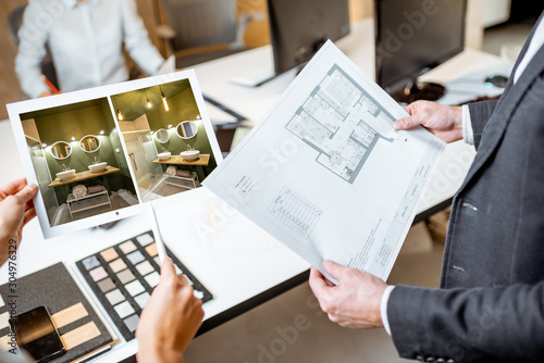 Creative office employees working on some architectural project, holding plans and interior renderings, close-up on the blueprints