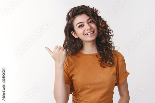 Girl inviting go together. Friendly charming smiling cute armenian woman tilting head pointing left thumb joyfully grinning asking you wanna visit cool place, recommending cafe, standing white wall