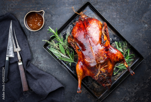 Traditional roasted stuffed Christmas Peking duck with herbs and sauce as top view on a rustic board