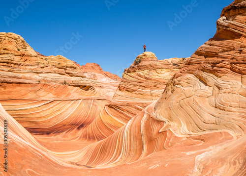 Man standing high above the Wave Formation on sandstone tower of orange and pink rock.
