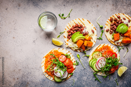 Open vegan tortilla wraps with sweet potato, beans, avocado, tomatoes, pumpkin and sprouts on gray background, flat lay, copy space. Healthy vegan food concept.