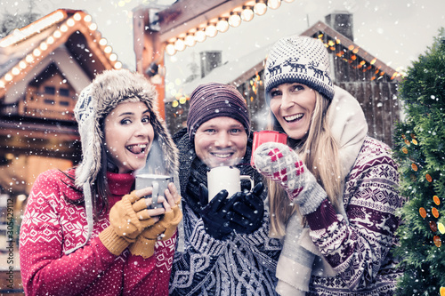 group of happy friends with hot drink on christmas market 