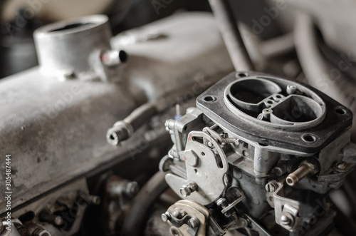 Engine compartment of an old car. Close-up view of a gasoline carburetor against a background of a car engine. Repair of an old car in a workshop. Selective focus. Blurred background.