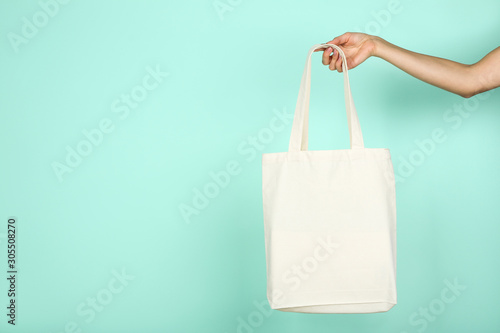 Female hand holding white cotton eco bag on mint background