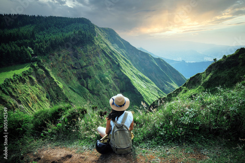 woman traveler holding hat and looking at amazing mountains and forest, wanderlust travel concept, space for text, atmospheric epic moment, azores ,portuhal, ponta delgada, sao miguel