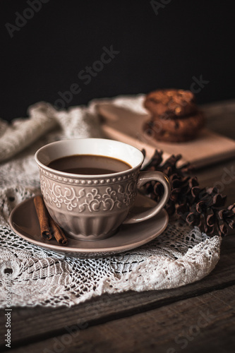 Hot coffee with cinnamon sticks and cookies on a wooden background