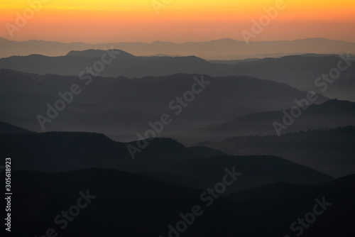 nature background with mountain silhouettes and a pine tree forest. Smooth gradient from dark to light orange caused by the long-focus lens and twilight. Carpathian mountains, Ukraine.