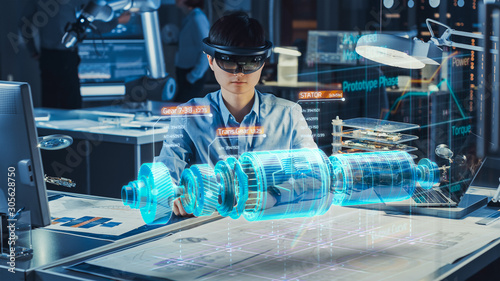 Industrial Factory Chief Engineer Wearing AR Headset Designs a Prototype of an Electric Motor on the Holographic Projection Blueprint. Futuristic Virtual Design of Mixed Technology Application.