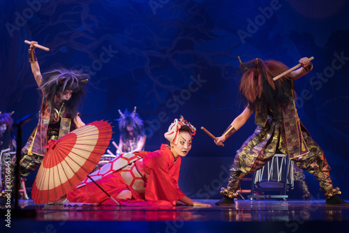 Traditional Japanese performance. Actress in traditional red kimono and fox mask lays down on the floor and demons dance around.