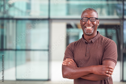 Portrait Of Smiling Mature Businessman Standing In Lobby Of Busy Modern Office