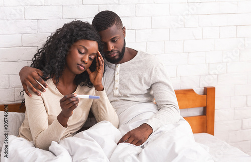 Black couple sitting on bed with negative pregnancy test result