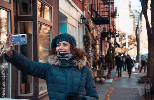 Beautiful curly brunette woman taking selfie self-portrait in Bleecker street, Greenwich Village, while sightseeing new york during winter season. Teal and orange color graded.