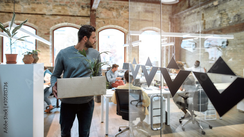 Saying good bye. Handsome man in casual wear holding box with personal things and leaving modern office