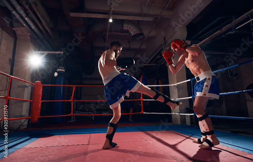 Two aggressive men boxers exercising kickboxing in the ring at the sport club
